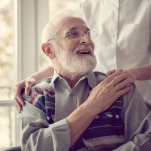 Senior man sitting on the wheelchair, laughing and holding his nurse's hand